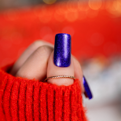 Unha com verniz roxo metálico em mão com camisola vermelha e anel dourado