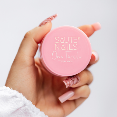 frasco rosa SAUTE NAILS em mão com unhas postiças decoradas