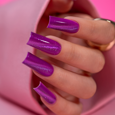 Unha com verniz roxo cintilante e forma quadrada em fundo rosa acolchoado