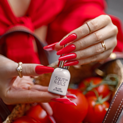 Frasco de verniz para unhas SAUTE NAILS Nº 557 LA TOMATINA com unhas vermelhas e tomates vermelhos ao fundo