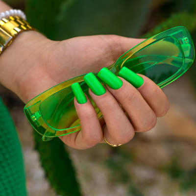 Mão com unhas verdes a segurar óculos de sol verdes transparentes