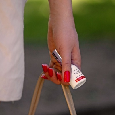 Mão segurando frasco de verniz de unhas branco com tampa metalizada