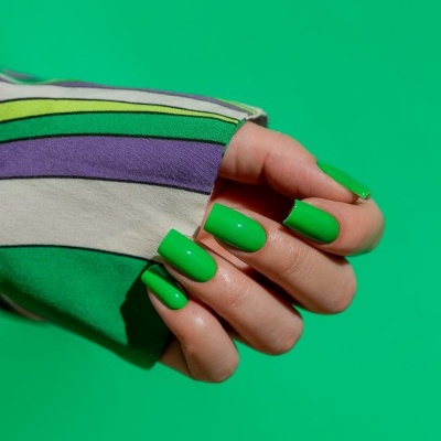 Unhas verdes vibrantes em mão segurando tecido com riscas coloridas