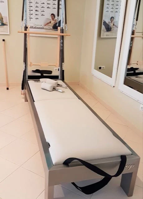 Cama de Pilates com colchão branco e barras pretas num estúdio com espelhos e pôsteres