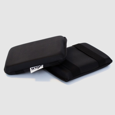 Dois apoios de pulso pretos com tecido liso e etiqueta branca num fundo cinzento claro