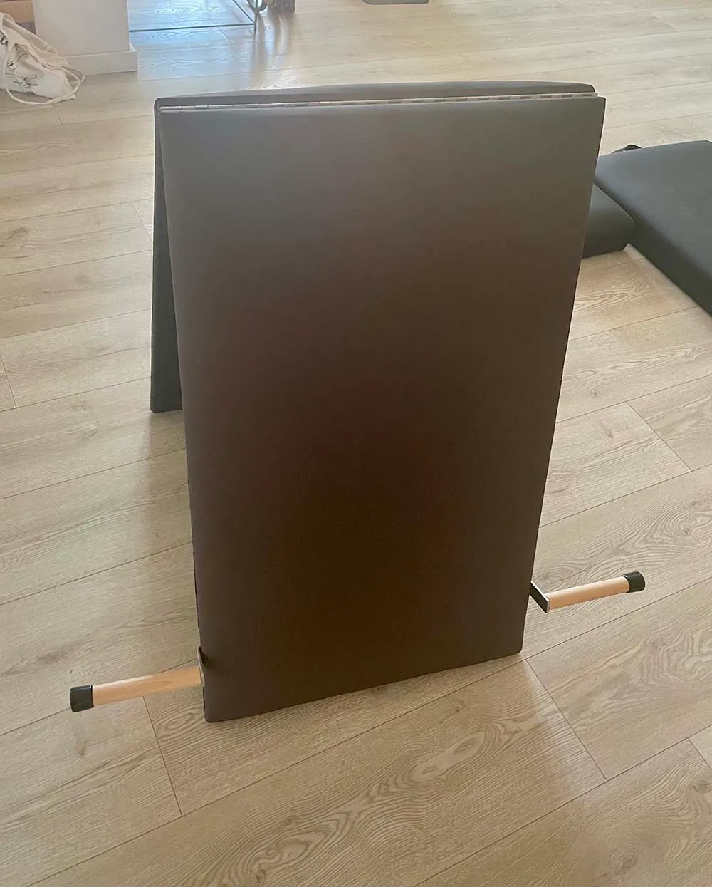 Colchão dobrável castanho com estrutura de madeira clara no chão de madeira clara