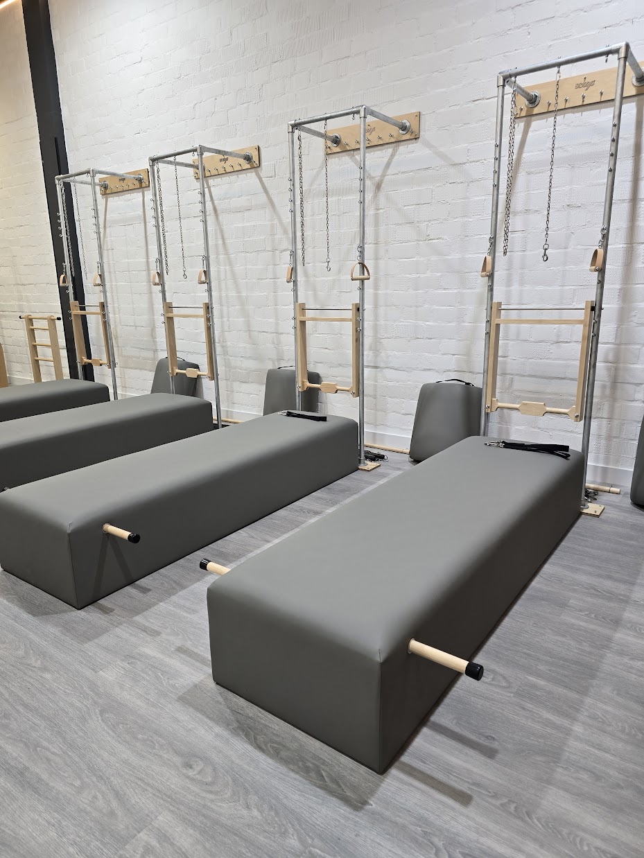 Conjunto de camas de Pilates com estrutura metálica, correntes e alças de madeira.