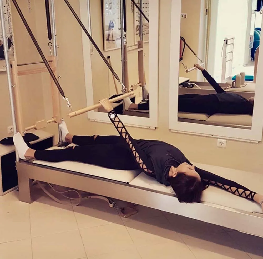 Pessoa a usar aparelho de Pilates em sala com espelhos