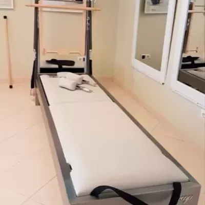 Cama de Pilates com colchão branco e barras pretas num estúdio com espelhos e pôsteres