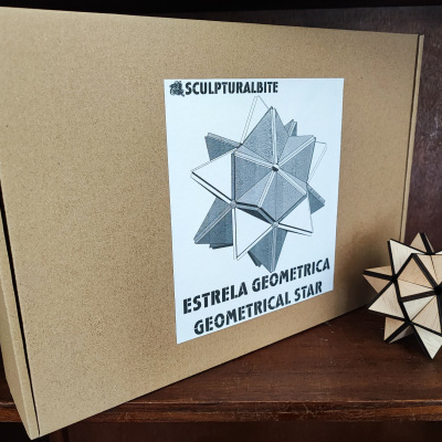 Caixa de cartão castanha com etiqueta branca e peça de madeira geométrica ao lado