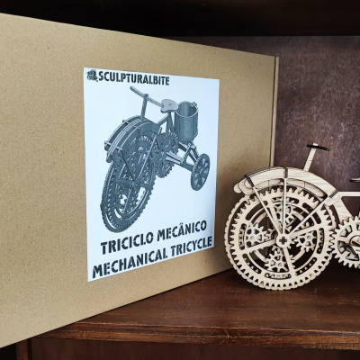 Modelo mecânico de triciclo em madeira clara com caixa de cartão castanha com etiqueta da marca SCULPTURAL.BITE