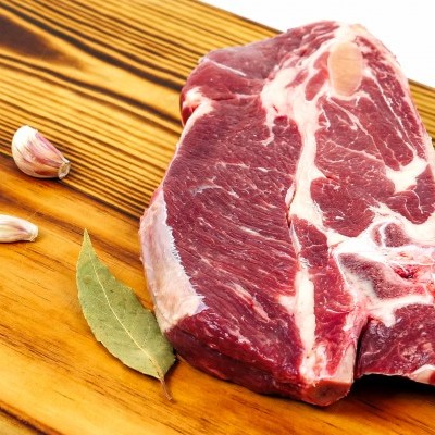 Bife cru com alho e folhas de louro numa tábua de madeira