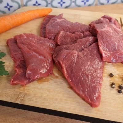 Pedaços de carne crua num tabuleiro de madeira com cenoura, salsa e pimenta