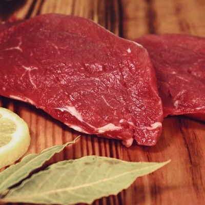 Duas peças de carne crua com uma fatia de limão e folhas de louro numa tábua de madeira