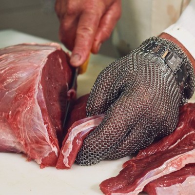 Mão com luva de malha metálica a cortar carne vermelha crua em fatias finas