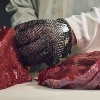 Mão com luva de malha de aço a segurar carne crua vermelha numa bancada