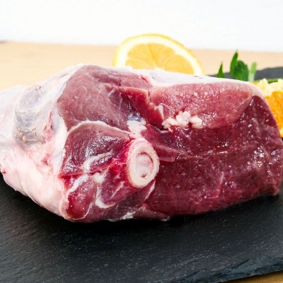 Peça de carne crua com osso sobre ardósia, acompanhada de limão, laranja e folhas verdes