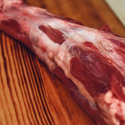 Peça grande de carne crua vermelha com gordura em cima de superfície de madeira.