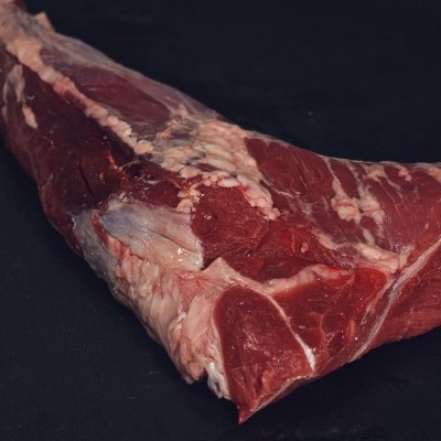 Peça de carne crua vermelha com gordura visível sobre superfície preta