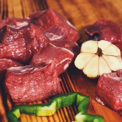 Cubos de carne crua, alho e pimento verde numa tábua de madeira