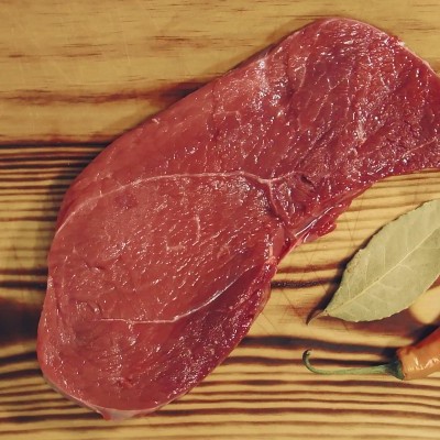 Bife cru vermelho com folha de louro e malagueta sobre tábua de madeira