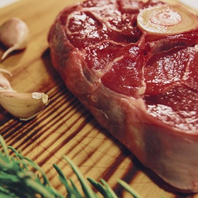 Carne crua com osso numa tábua de madeira com alho e alecrim
