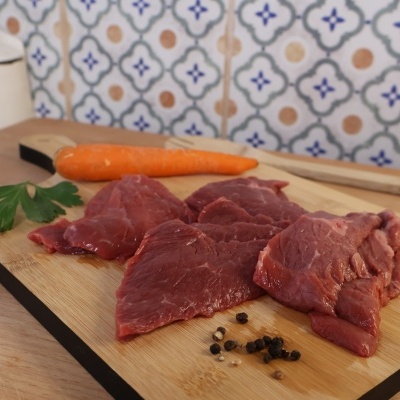 Pedaços de carne crua numa tábua de madeira com cenoura e especiarias