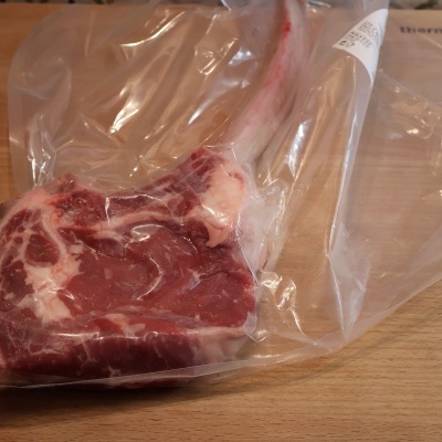 Bife cru com osso embalado a vácuo sobre superfície de madeira