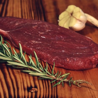 Bife cru com alecrim e alho numa tábua de madeira