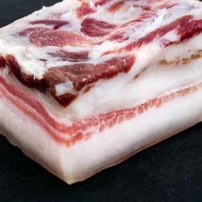 Bloco de toucinho cru com gordura branca e carne vermelha numa superfície escura.