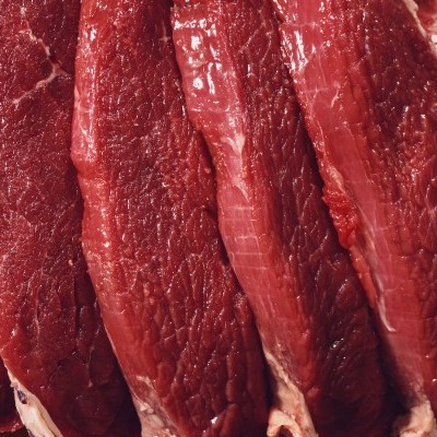 Fatias de carne crua vermelha com textura fibrosa sobre superfície de madeira