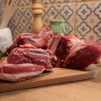 Três pedaços de carne crua sobre tábua de madeira num balcão com azulejos decorativos ao fundo