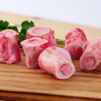 Seis ossos crus vermelhos e brancos numa tábua de madeira com um ramo de salsa ao fundo