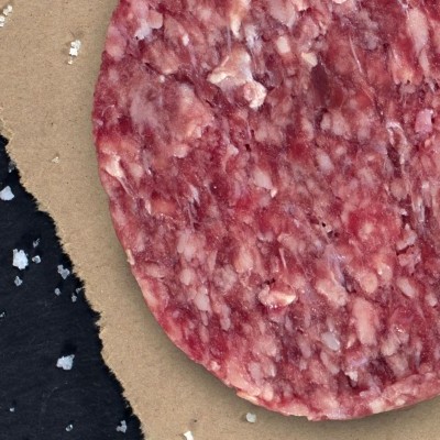 Fatias redondas de carne moída crua sobre papel castanho com sal grosso