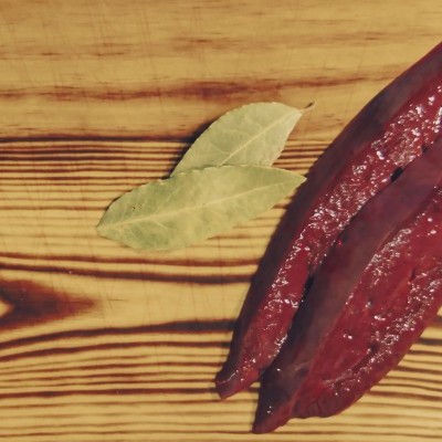 Dois pedaços de carne vermelha crua numa tábua de madeira com folhas de louro verdes.