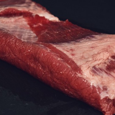 Pedaço de carne crua vermelha com gordura branca sobre superfície preta