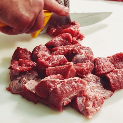 Carne crua vermelha sendo cortada em cubos com faca de cabo amarelo