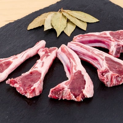 Cinco costeletas cruas com folhas de louro numa tábua preta