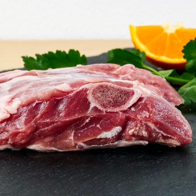 Pedaço de carne crua com osso sobre superfície preta com folhas verdes e fatia de laranja