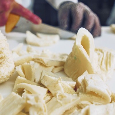 Tripas de porco em processo de corte por mãos com luva metálica em superfície branca