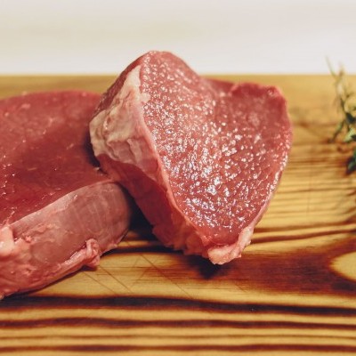 Dois bifes crus sobre tábua de madeira com ervas