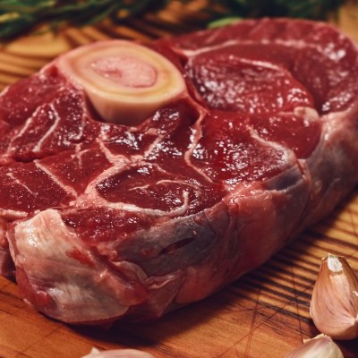 Bife cru com osso e alho sobre tábua de madeira com alecrim