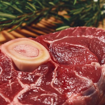 Peça crua de carne vermelha com osso sobre tábua de madeira e folhas verdes