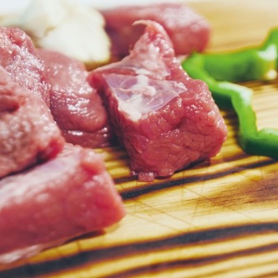 Cubos de carne crua ao lado de fatias de pimento verde numa tábua de madeira