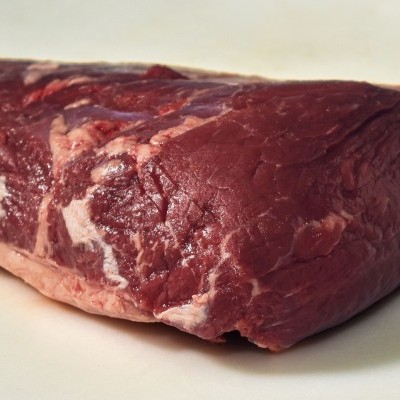 Peça de carne crua vermelha com gordura branca sobre superfície clara