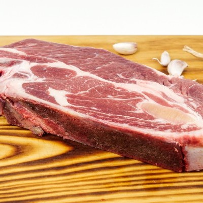 Pedaço cru de carne vermelha com gordura branca numa tábua de madeira com alho ao fundo