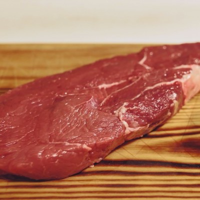 Fatias de carne crua vermelha e pedaço de pimento verde sobre tábua de madeira