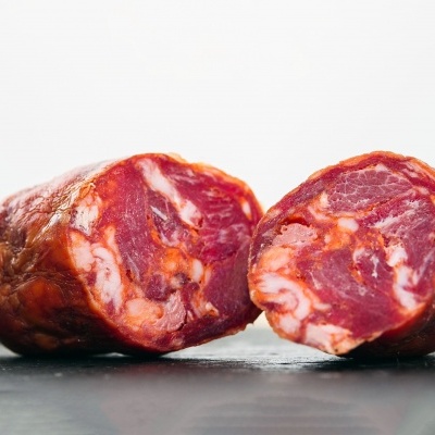 Chouriço cortado ao meio com textura visível e fundo neutro