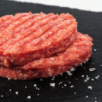 Dois hambúrgueres crus de carne na superfície preta com sal grosso