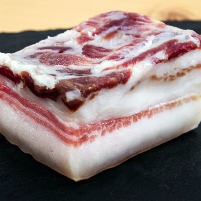 Pedaço de toucinho cru com camadas de gordura e carne em prato preto